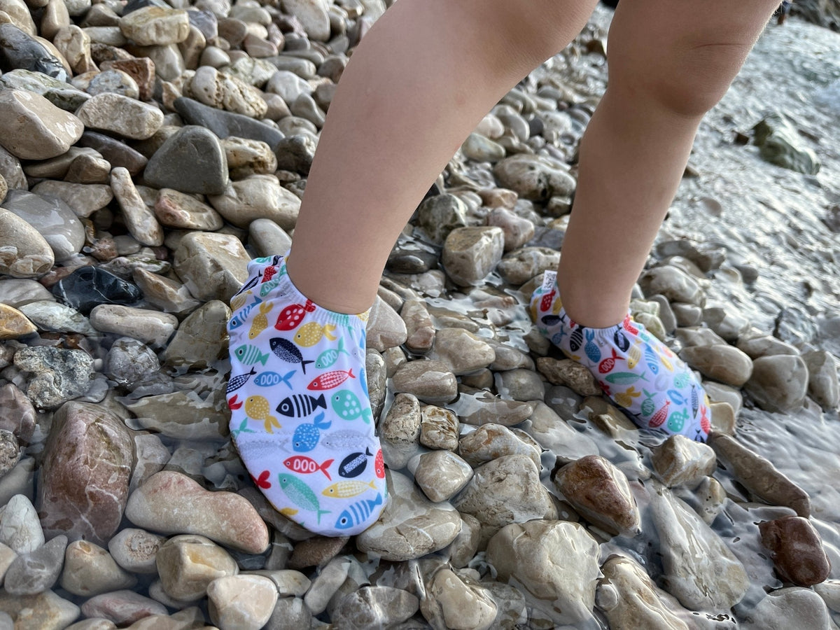 Side view of colorful fish-print water shoes worn on a pebble beach.