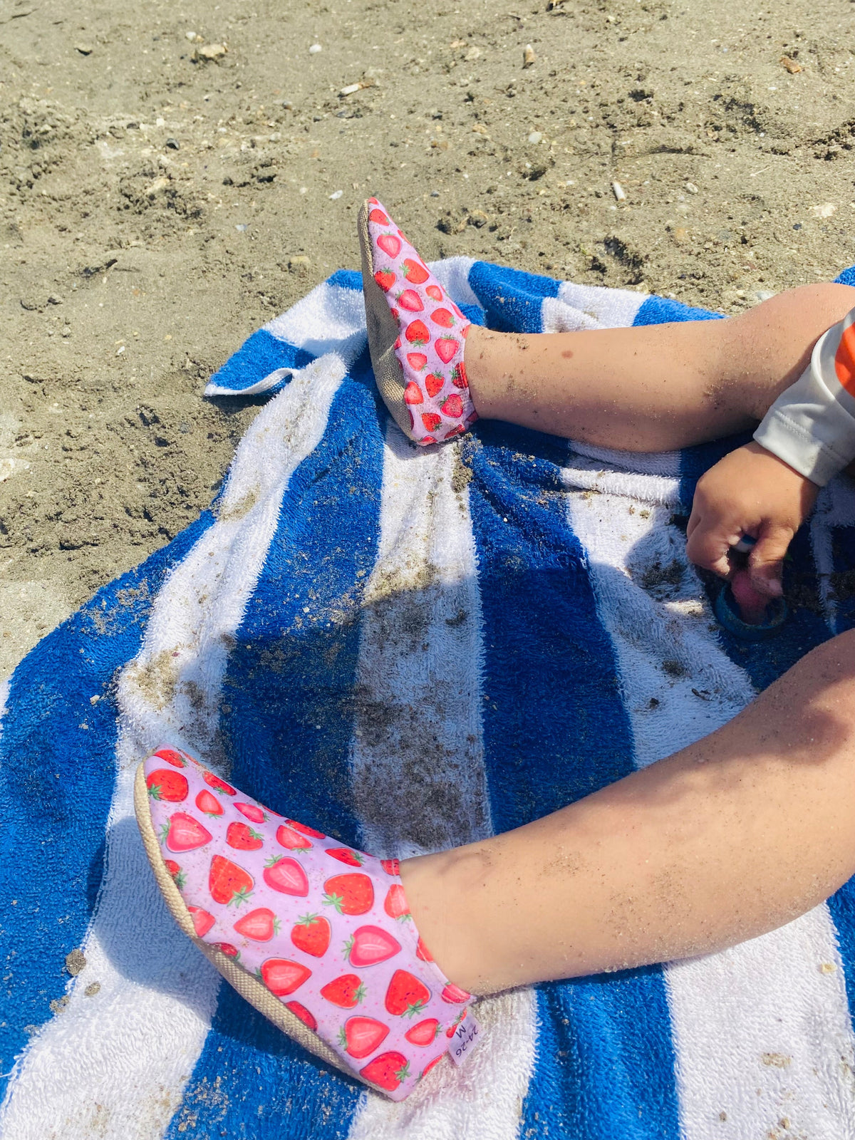 Close-up of strawberry-print water shoes worn on a striped beach towel.