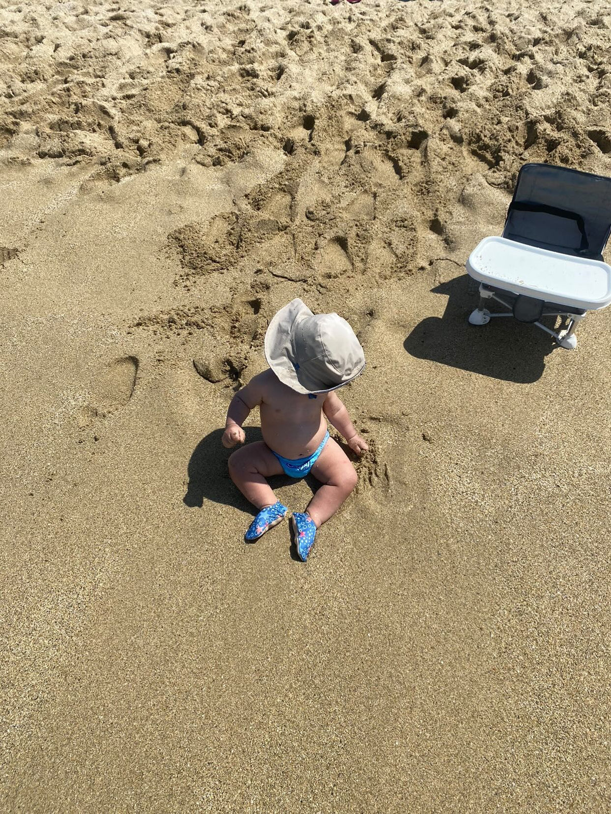 Overhead view of a child standing on sand wearing starfish-print water shoes.