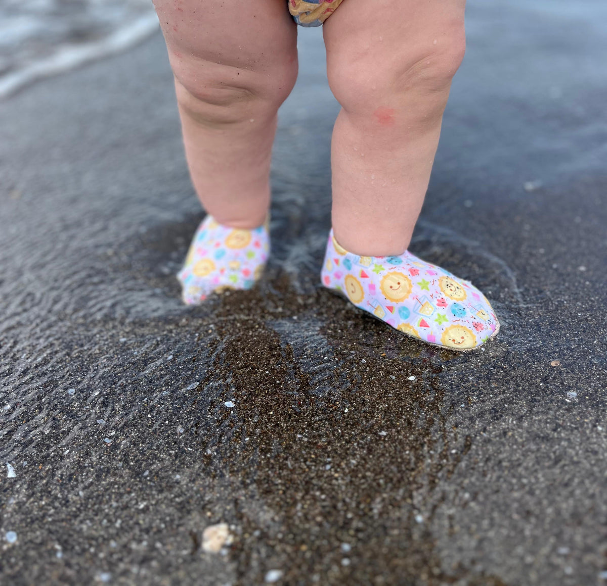 Close-up of sun-print water shoes worn on wet sand.