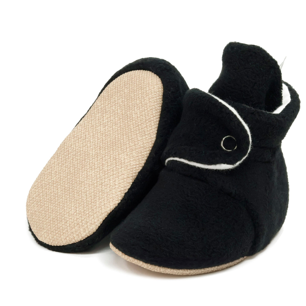 Black fleece-texture baby booties with snap straps and tan soles, with one sole facing the camera on a white background.