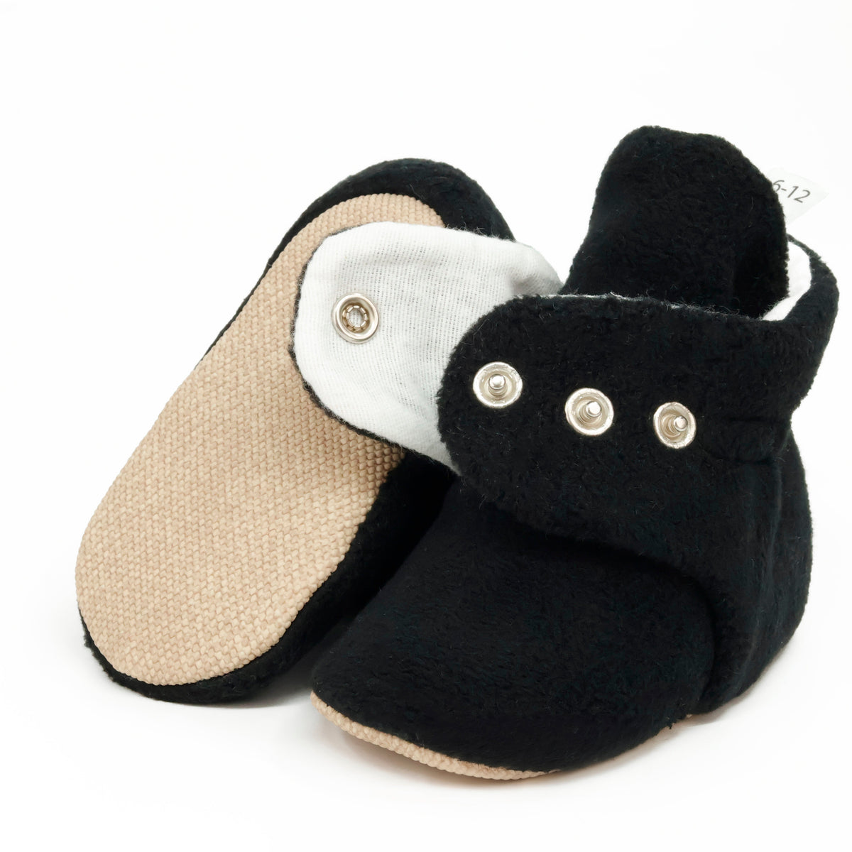 Black fleece-texture baby booties with snap straps and tan soles, showing one sole and an open snap strap on white.