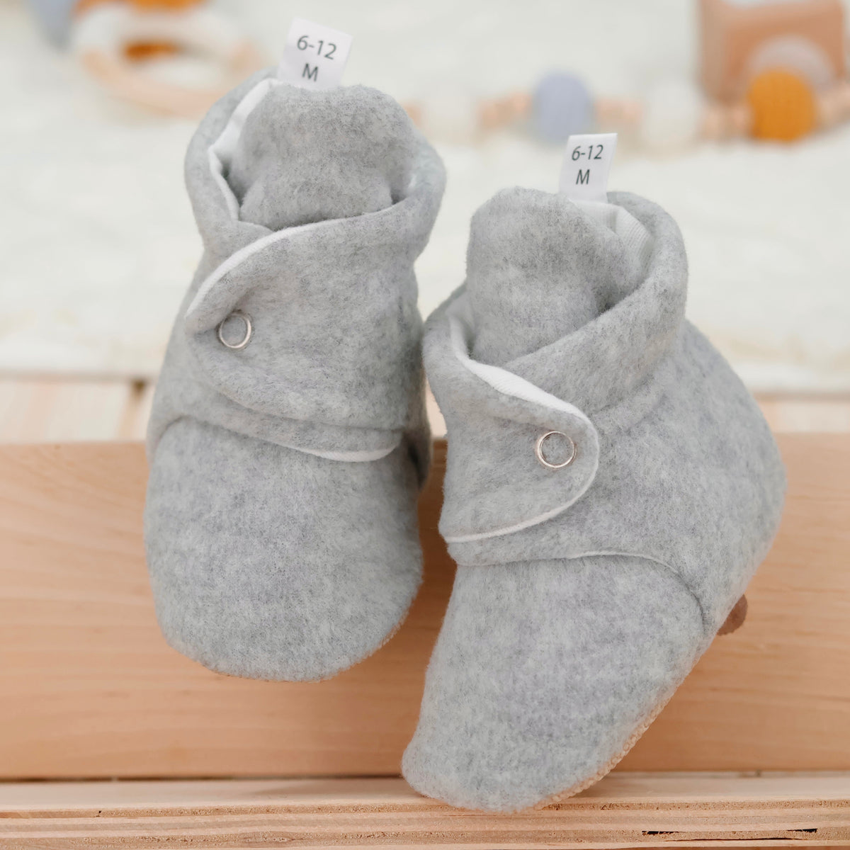Front view of a pair of light gray fleece-texture baby booties with snap straps and tan soles.