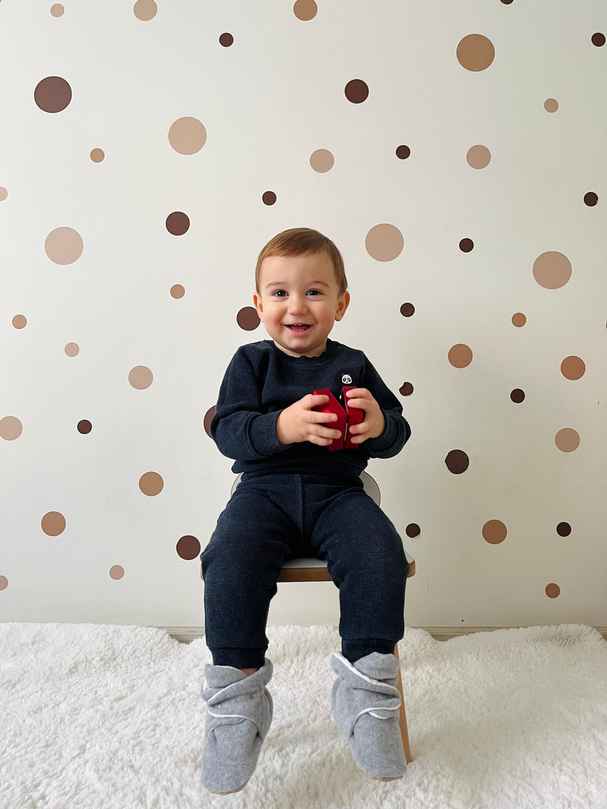 Child seated on a couch wearing gray booties, front view.