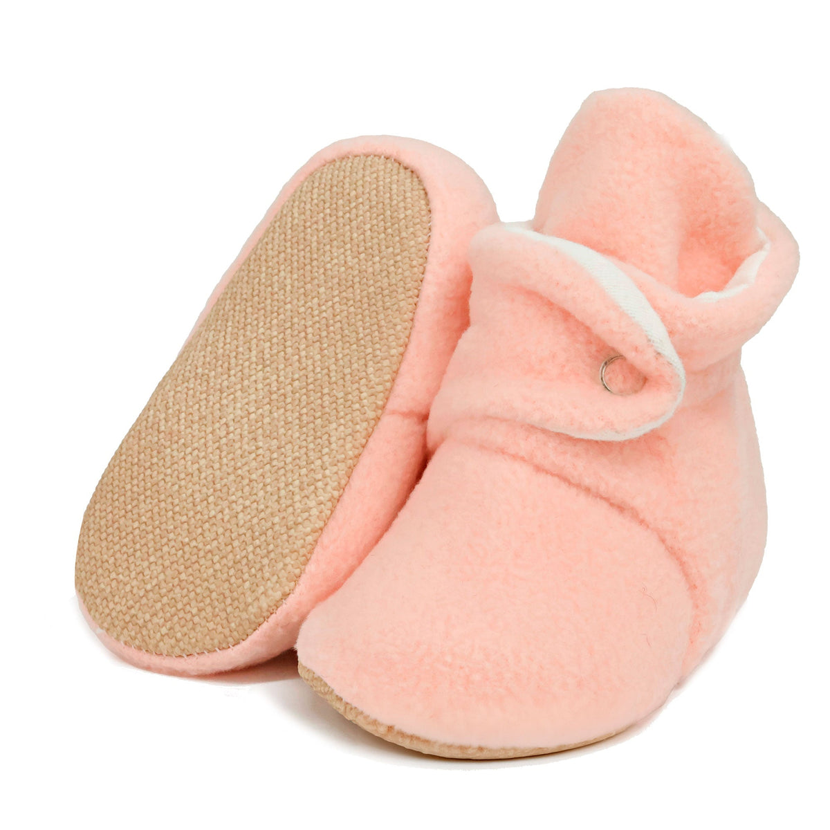 Pale pink fleece-texture baby booties with snap straps and tan soles, with one sole facing the camera on a white background.