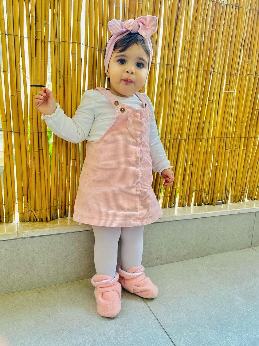 Child standing in front of a gold backdrop wearing pink booties.