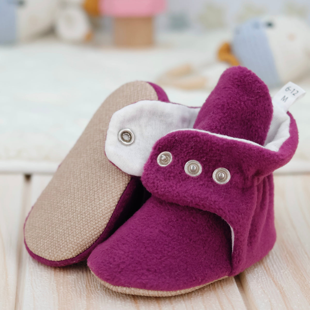 Close-up of purple fleece-texture baby booties with snap straps and tan soles, showing one sole and an open snap strap.