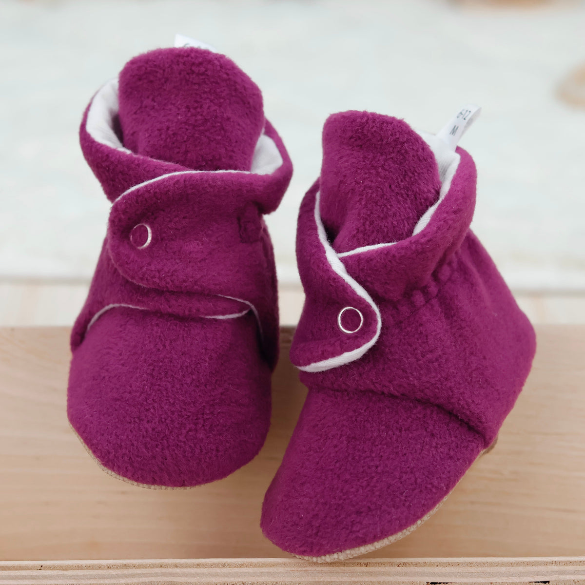 Front view of a pair of purple fleece-texture baby booties with snap straps and tan soles.