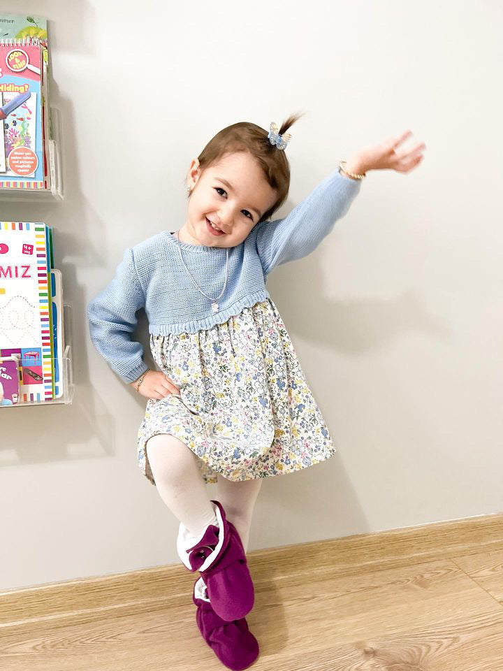 Child standing against a wall wearing purple booties.