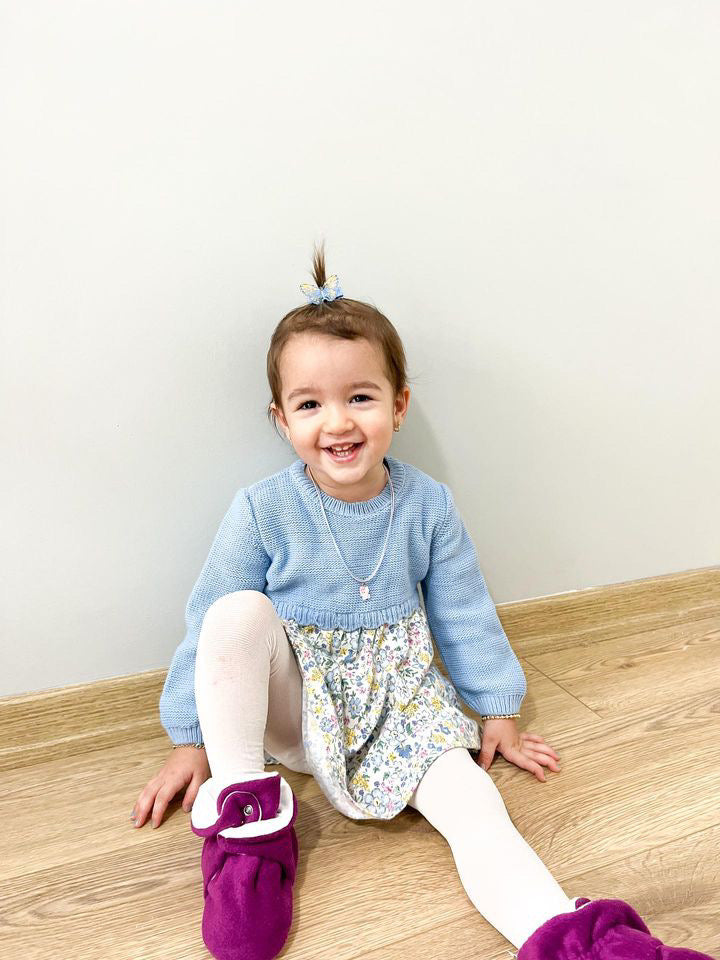 Child seated smiling with purple booties visible.