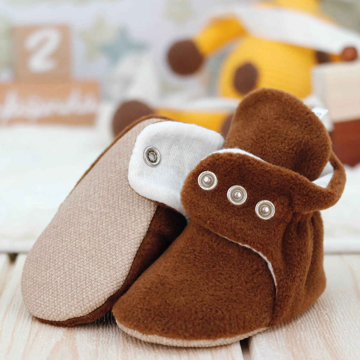 Close-up of warm brown fleece-texture baby booties with snap straps and tan soles, showing one sole and an open snap strap.