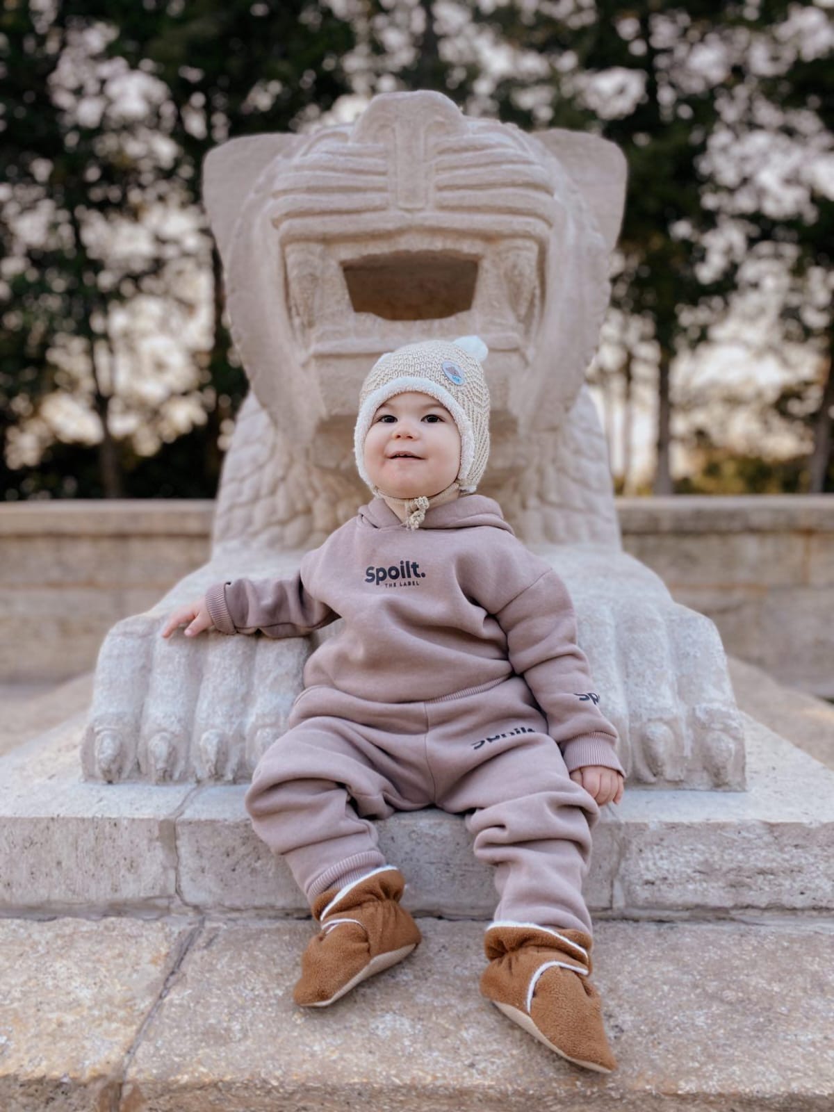 Baby seated on an ornate outdoor chair wearing brown booties.