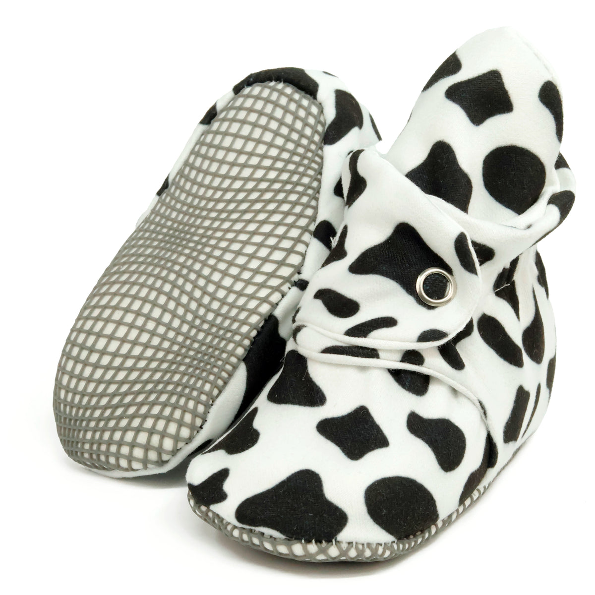 White baby booties with black cow spots and snap straps, with one sole facing the camera on a white background.