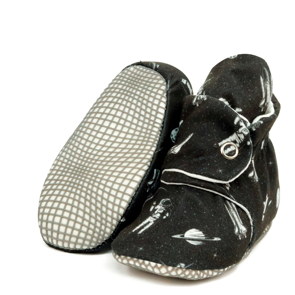 Black baby booties with white space motifs and snap straps, with one sole facing the camera on a white background.