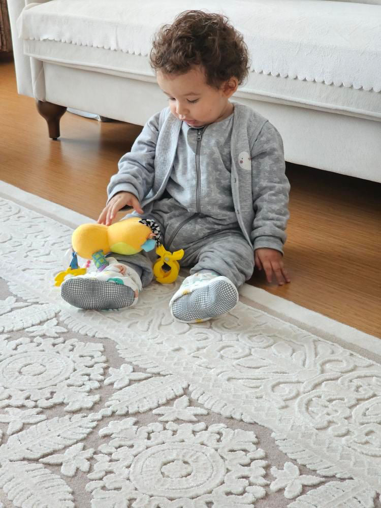Child seated on a rug holding a toy and wearing elephant-print booties.