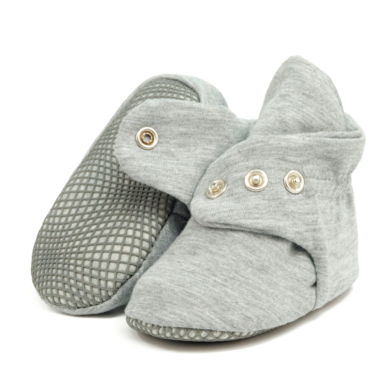 Light gray fabric baby booties with snap straps and gray grip soles, showing one sole and an open snap strap on white.