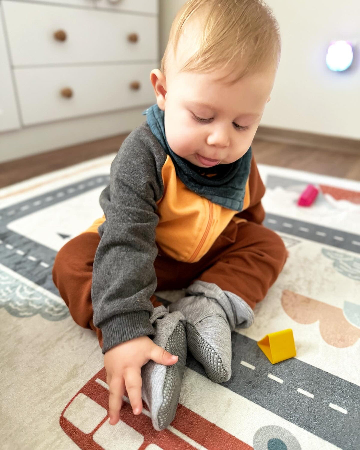 Child seated on a road-pattern rug wearing gray booties.