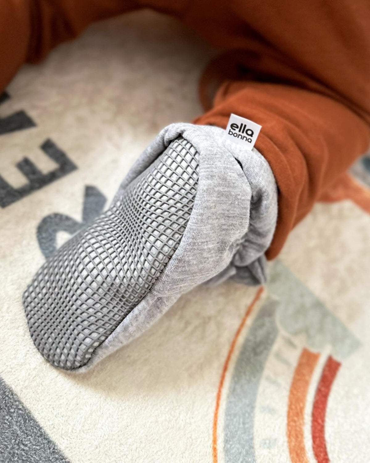 Close-up of a gray bootie sole worn with rust-colored trousers.