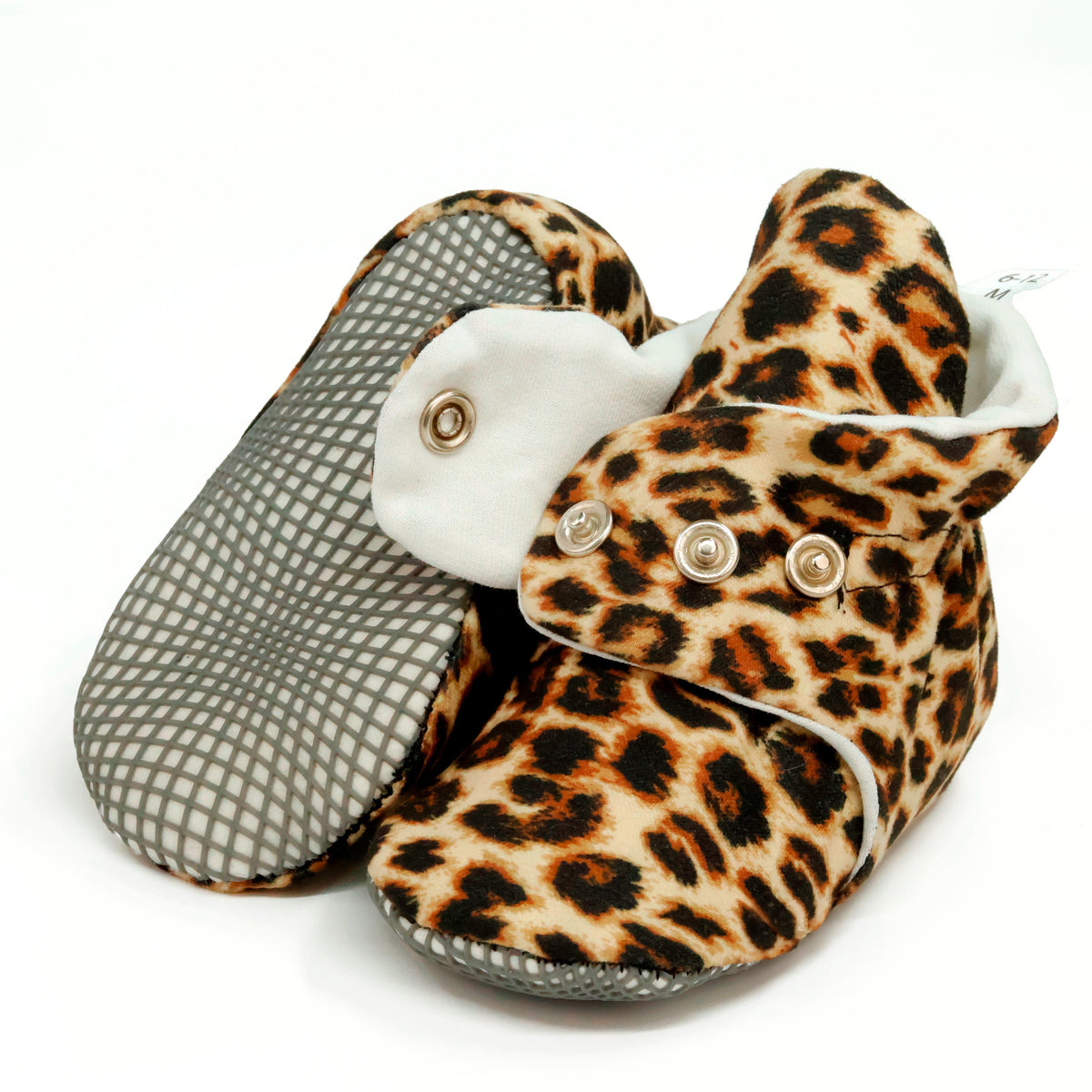 Tan baby booties with brown-and-black leopard spots and snap straps, showing one sole and an open snap strap on white.