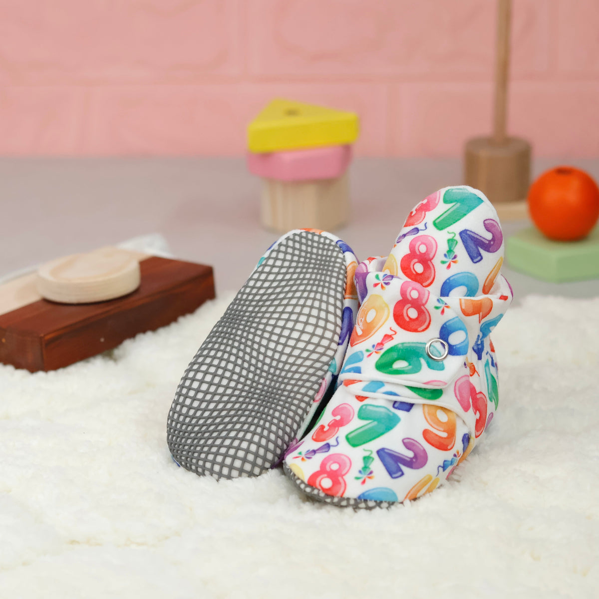 White baby booties with colorful numbers and snap straps arranged on a surface with one sole facing the camera.