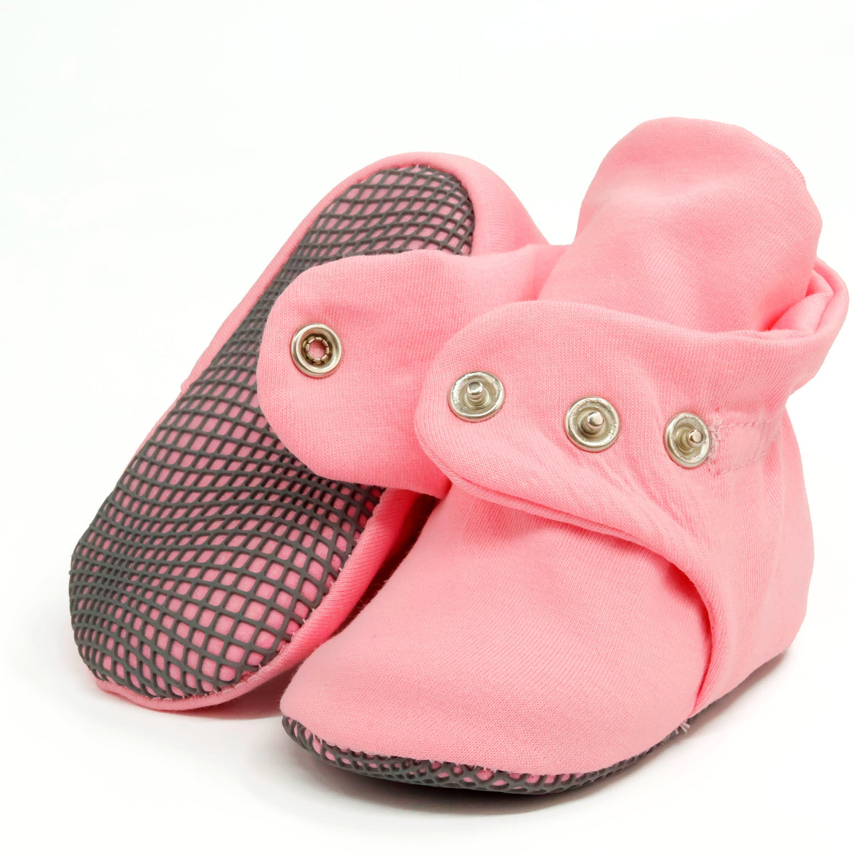 Pink fabric baby booties with snap straps and gray grip soles, showing one sole and an open snap strap on white.