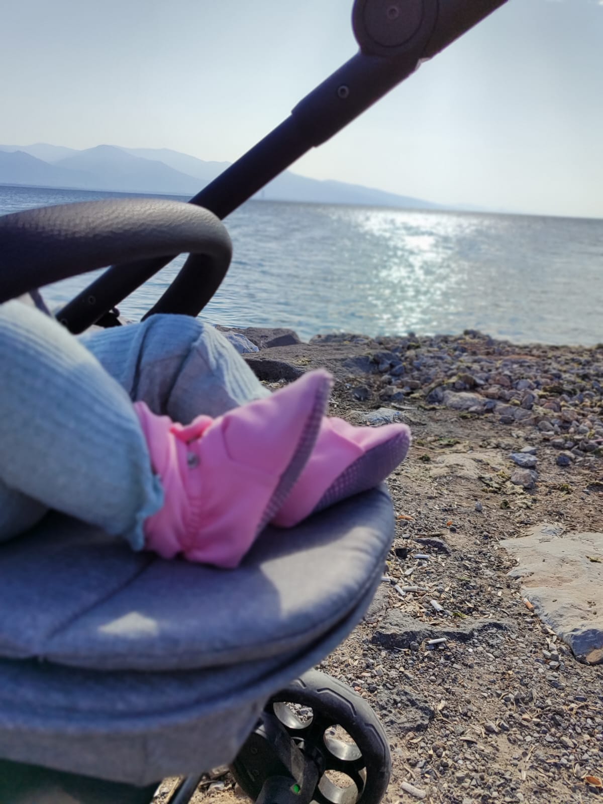 Pink booties worn in a stroller beside the sea, side view.