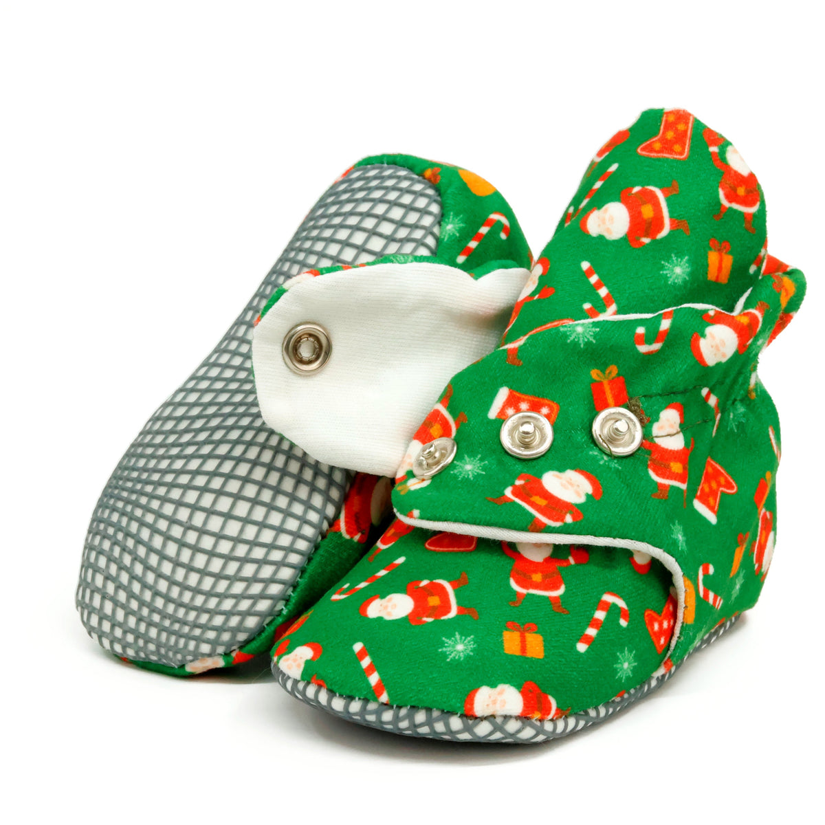 Green baby booties with Santa Claus Christmas print and snap straps, showing one sole and an open snap strap on white.