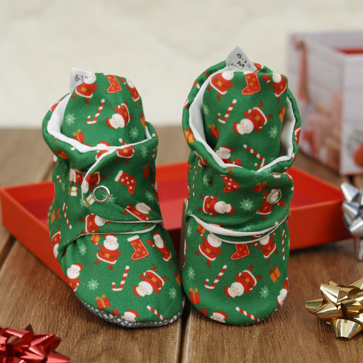 Front view of a pair of green baby booties with Santa Claus Christmas print and snap straps.