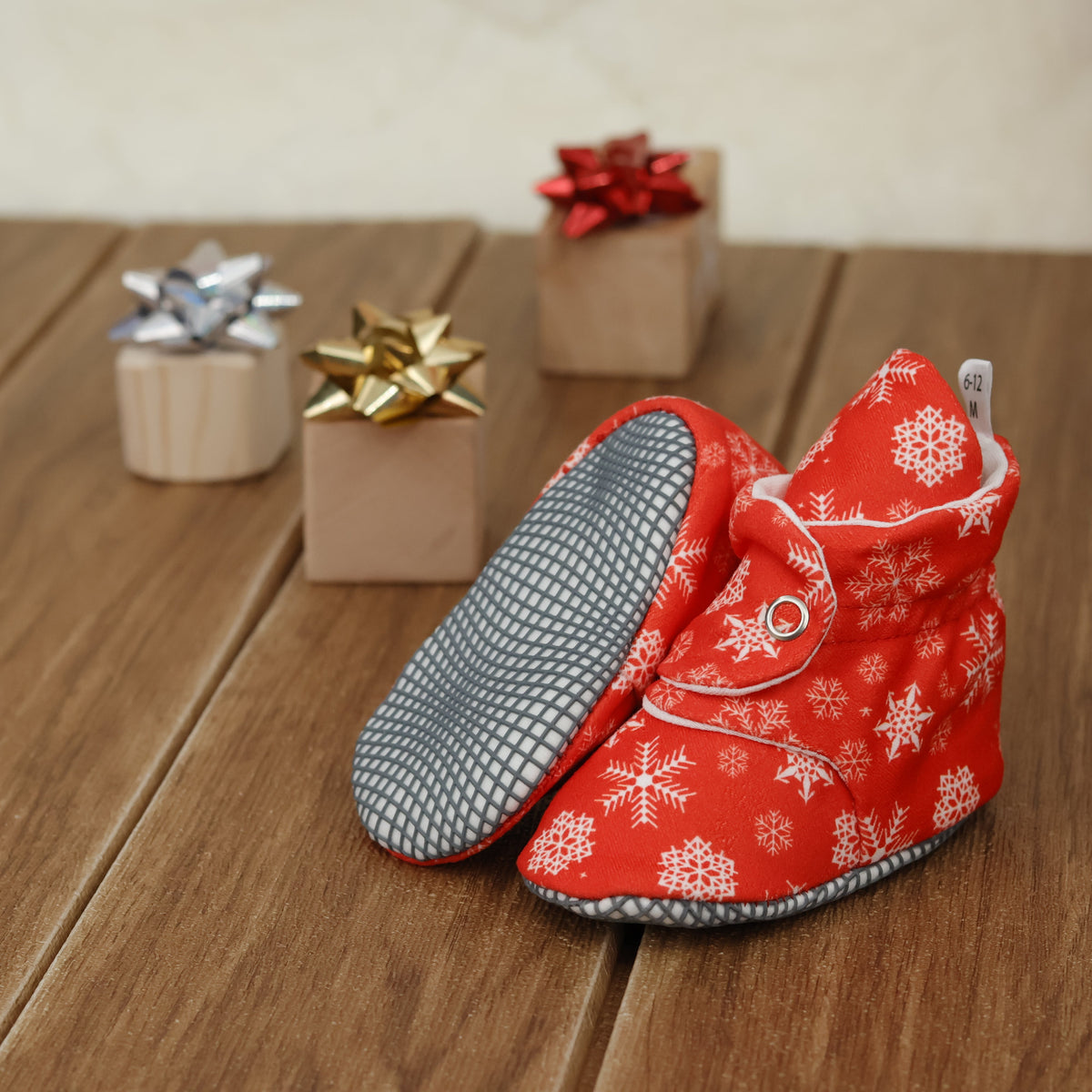 Red baby booties with white snowflakes and snap straps arranged on a surface with one sole facing the camera.