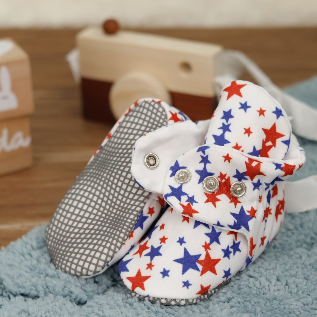 Close-up of white baby booties with red-and-blue stars and snap straps, showing one sole and an open snap strap.
