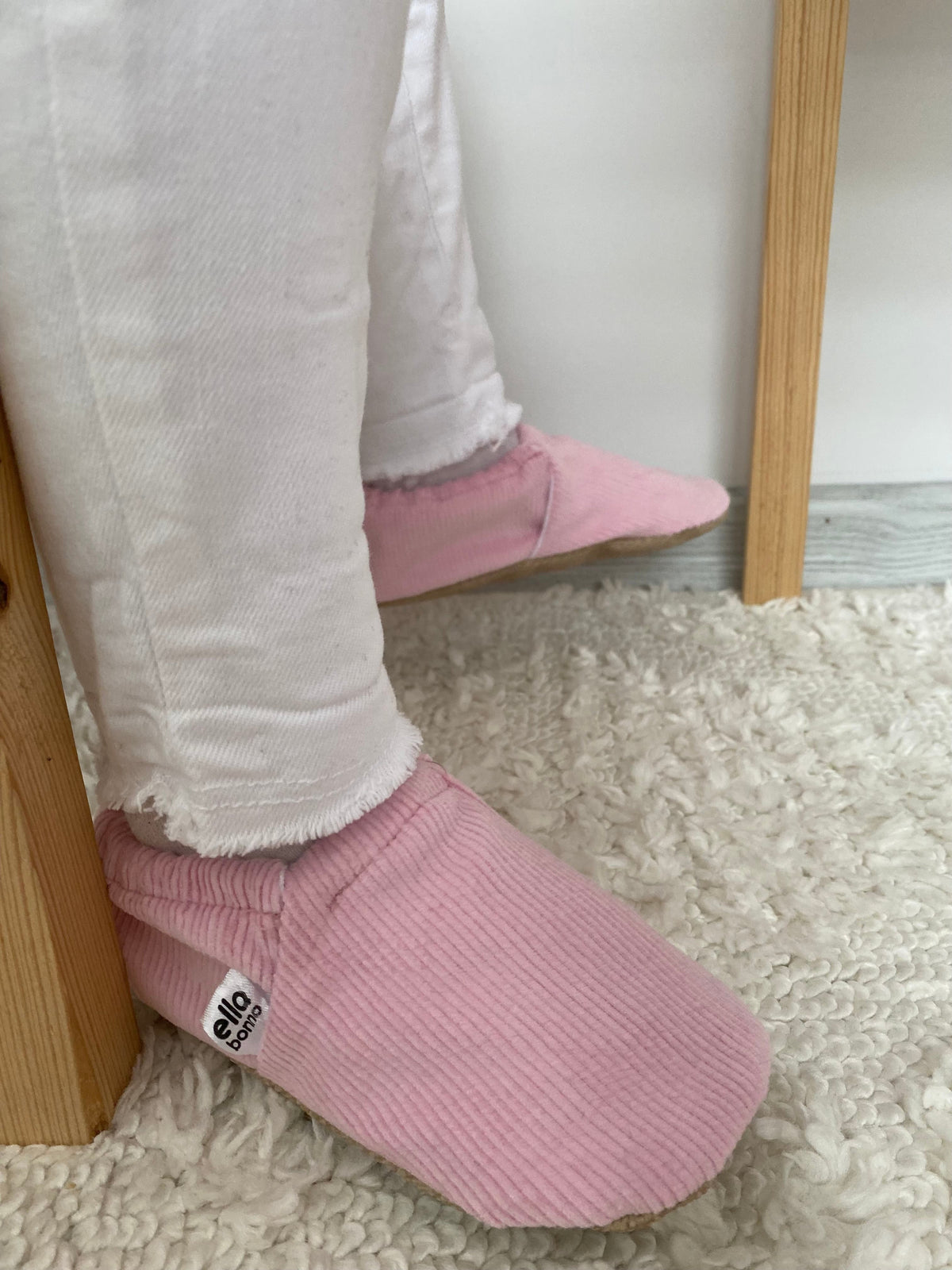 Side close-up of pink corduroy moccasins worn with pale trousers.
