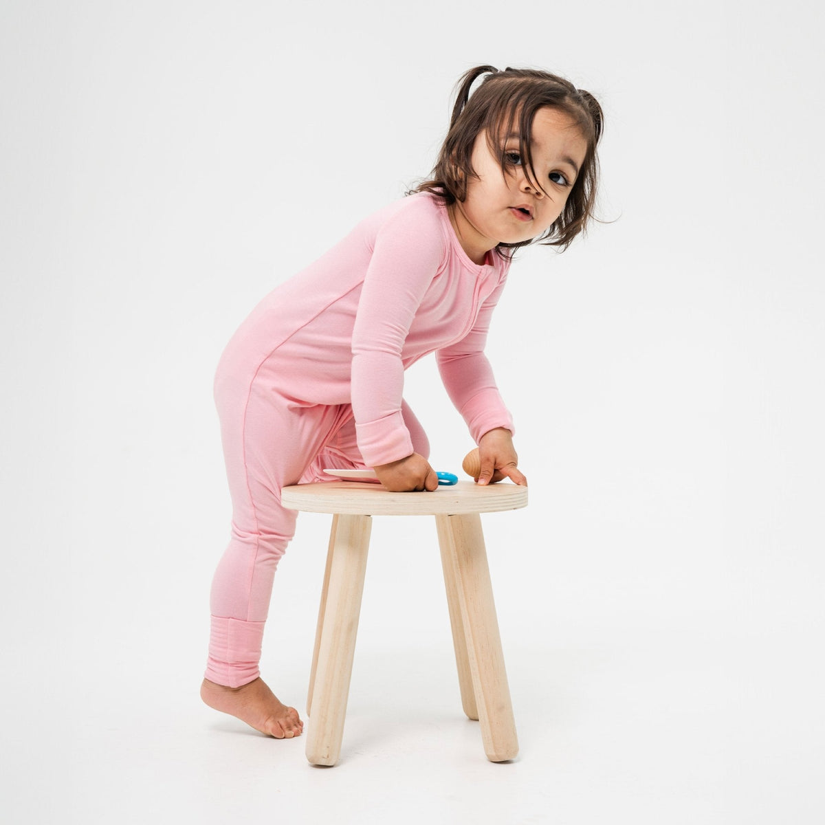 Child leaning on a wooden stool while wearing Bam & Stitch Pink Blossom Convertible Romper.