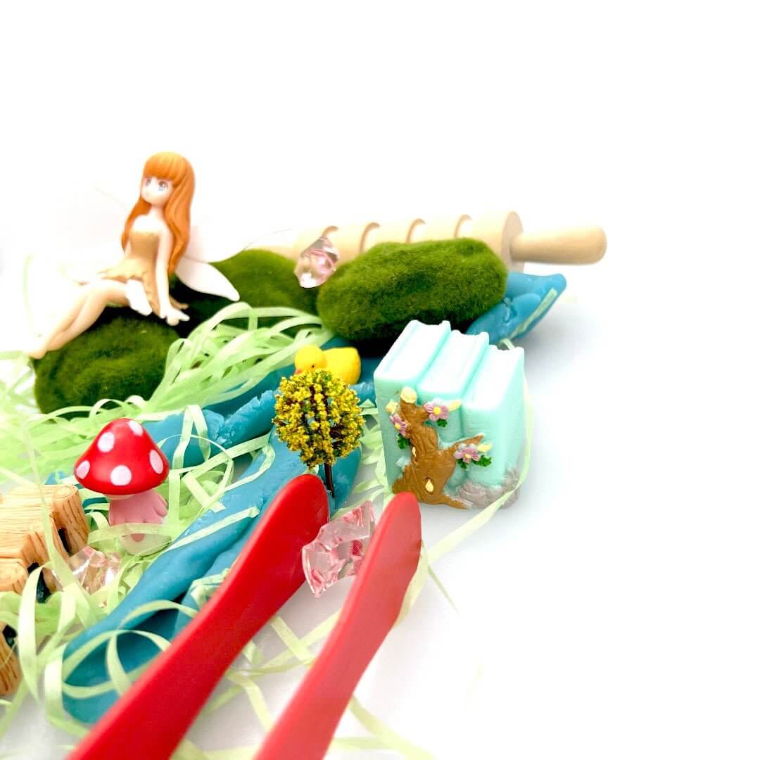 Red tongs holding a pink gem beside the Pixie Hollow fairy scene