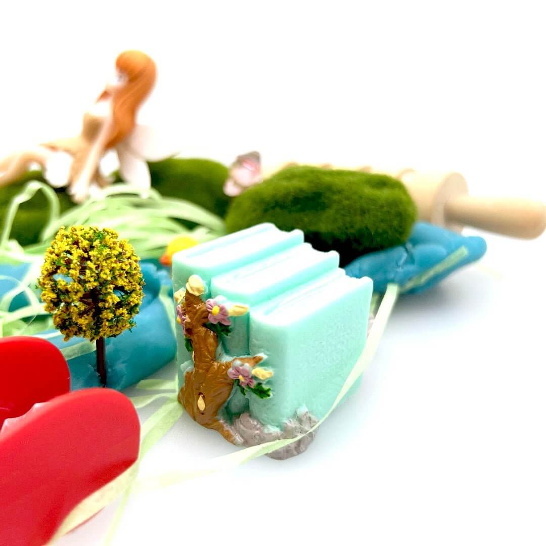 Book-shaped fairy house and miniature tree beside red tongs in the Pixie Hollow kit