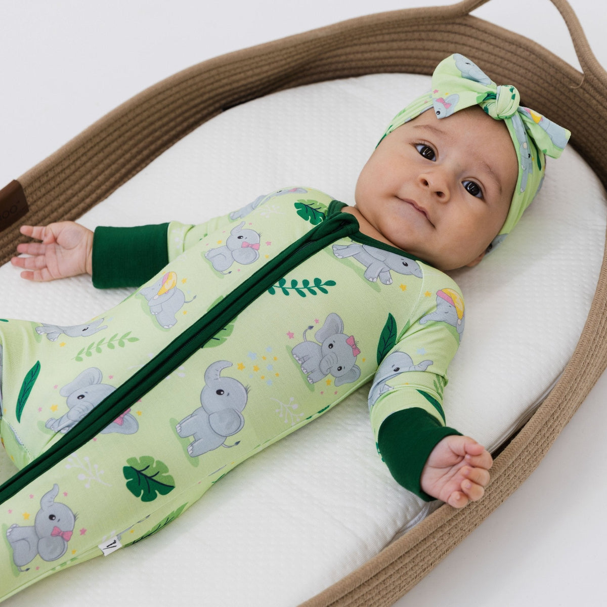 Baby lying in a basket wearing Bam & Stitch Playfully Strong Convertible Romper, with a coordinating bow headband.