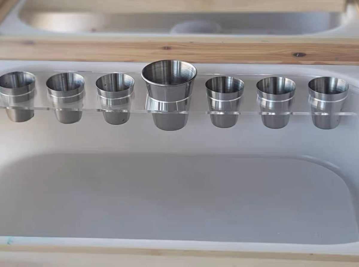 Seven stainless steel cups arranged across a sensory bin
