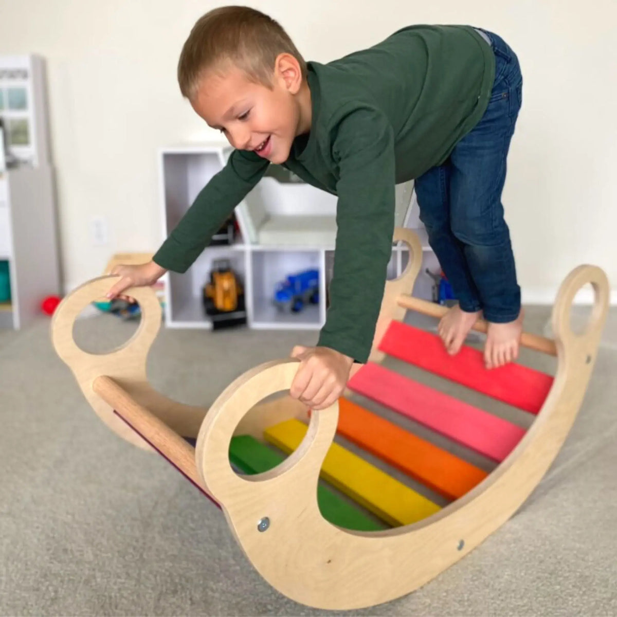 Child crouching on a rainbow-slat rocker and gripping the circular handles.