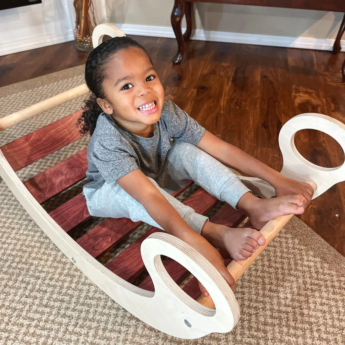 Child sitting in a reddish-brown-slat rocker with circular handles.