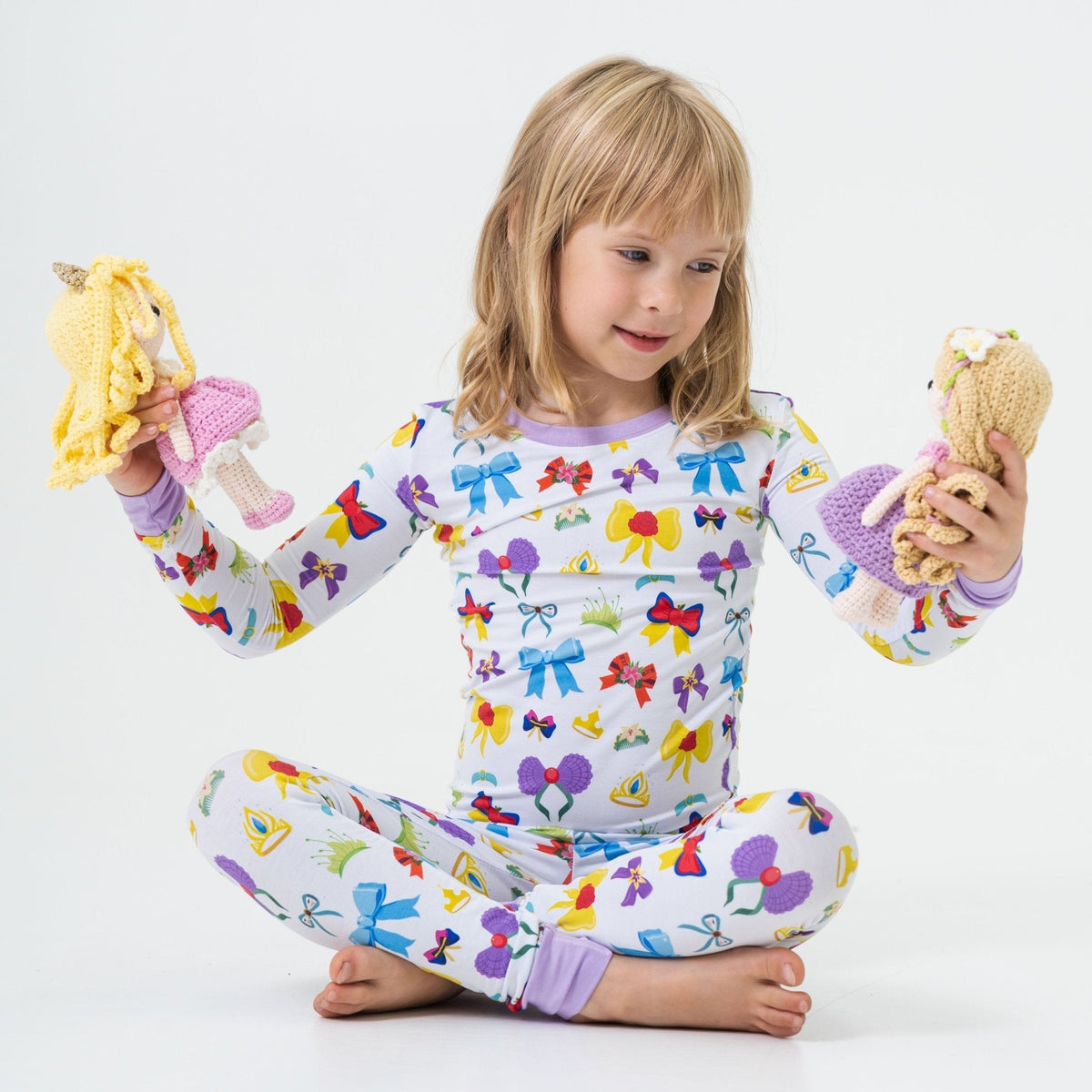 Child seated with a soft toy while wearing Bam & Stitch Sparkle & Reign Long Sleeve Pajamas.
