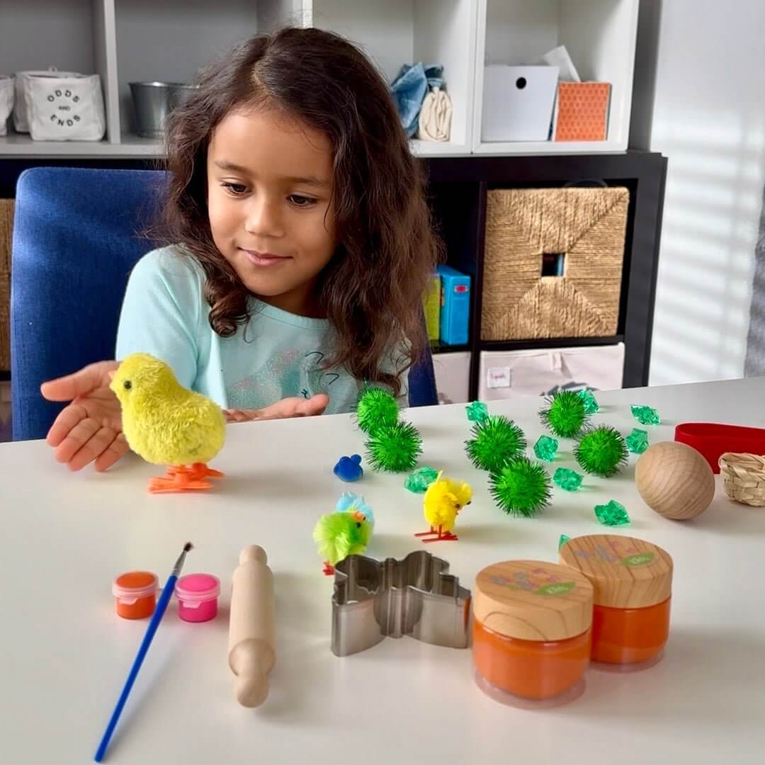 Child playing with Spring Garden chicks beside playdough jars, cutters and painting tools