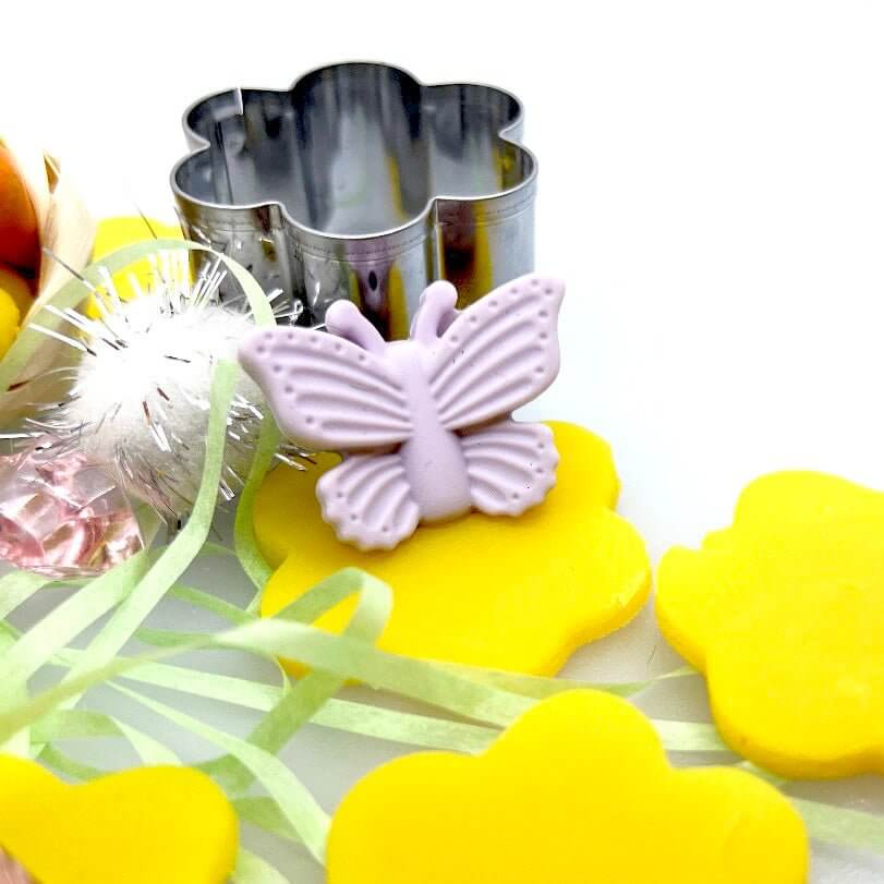 Purple butterfly decoration and flower cutter beside yellow playdough flowers