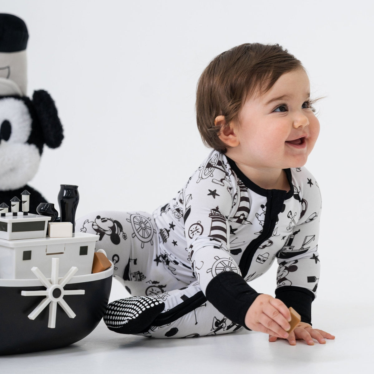 Baby playing while seated in Bam & Stitch Steamboat Willie Convertible Romper.