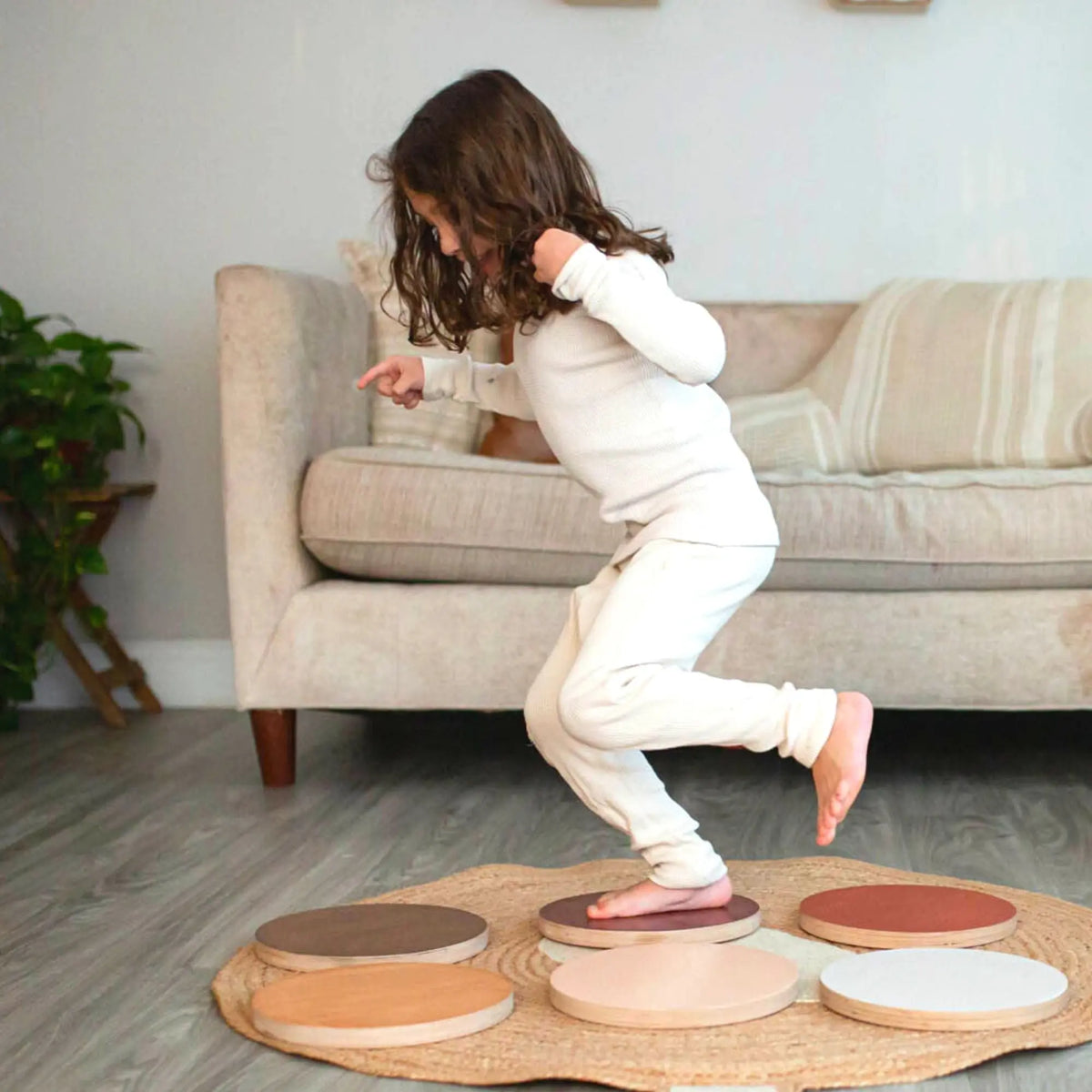 Child stepping across round brown, cream and reddish stepping stones on a bear-shaped rug.