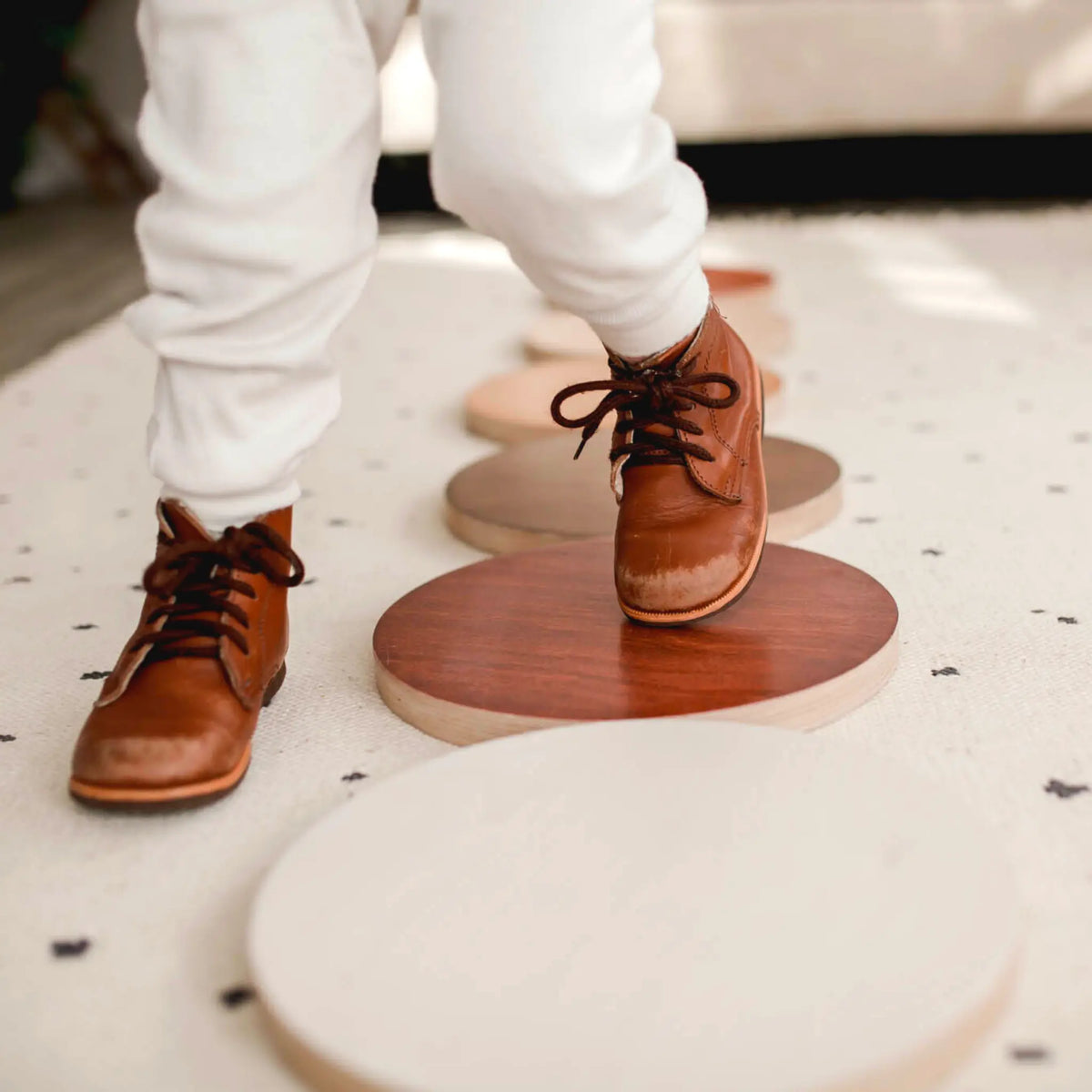 Close-up of a child in brown boots stepping on a reddish-brown round stepping stone.