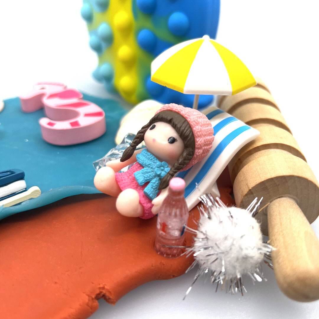 Miniature doll in a striped beach chair beside an umbrella in the Surf & Sand playdough scene