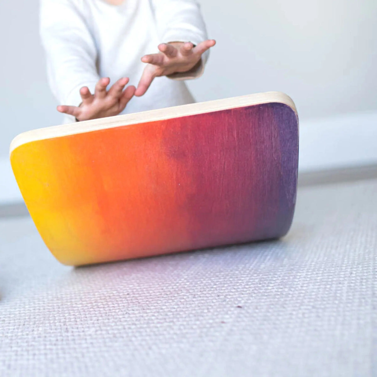Close-up of a child's hands above a wobble board with a yellow, red and purple gradient.
