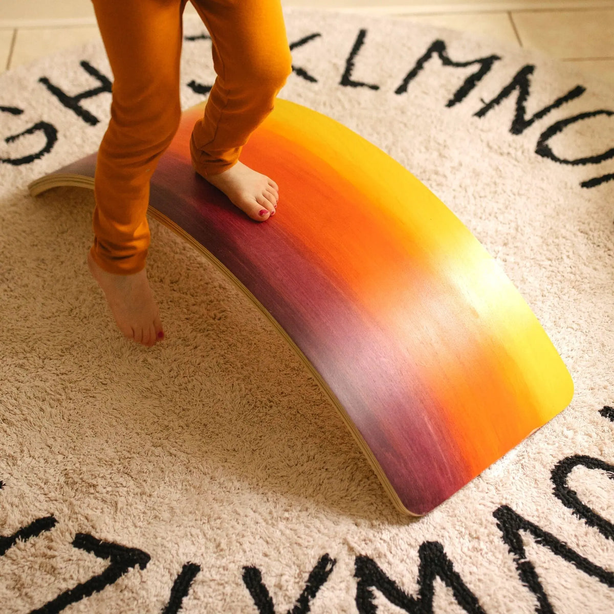 Close-up of bare feet standing on the arch of a yellow, orange, red and purple wobble board.