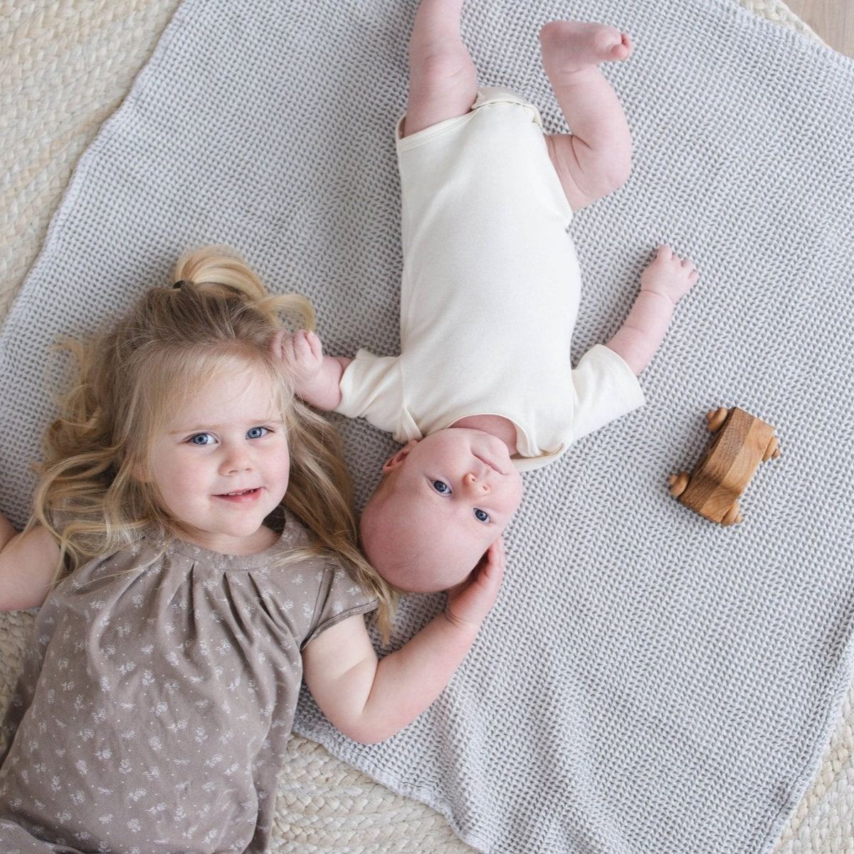 SpiritnSprout: Two children lying together on a grey waffle blanket