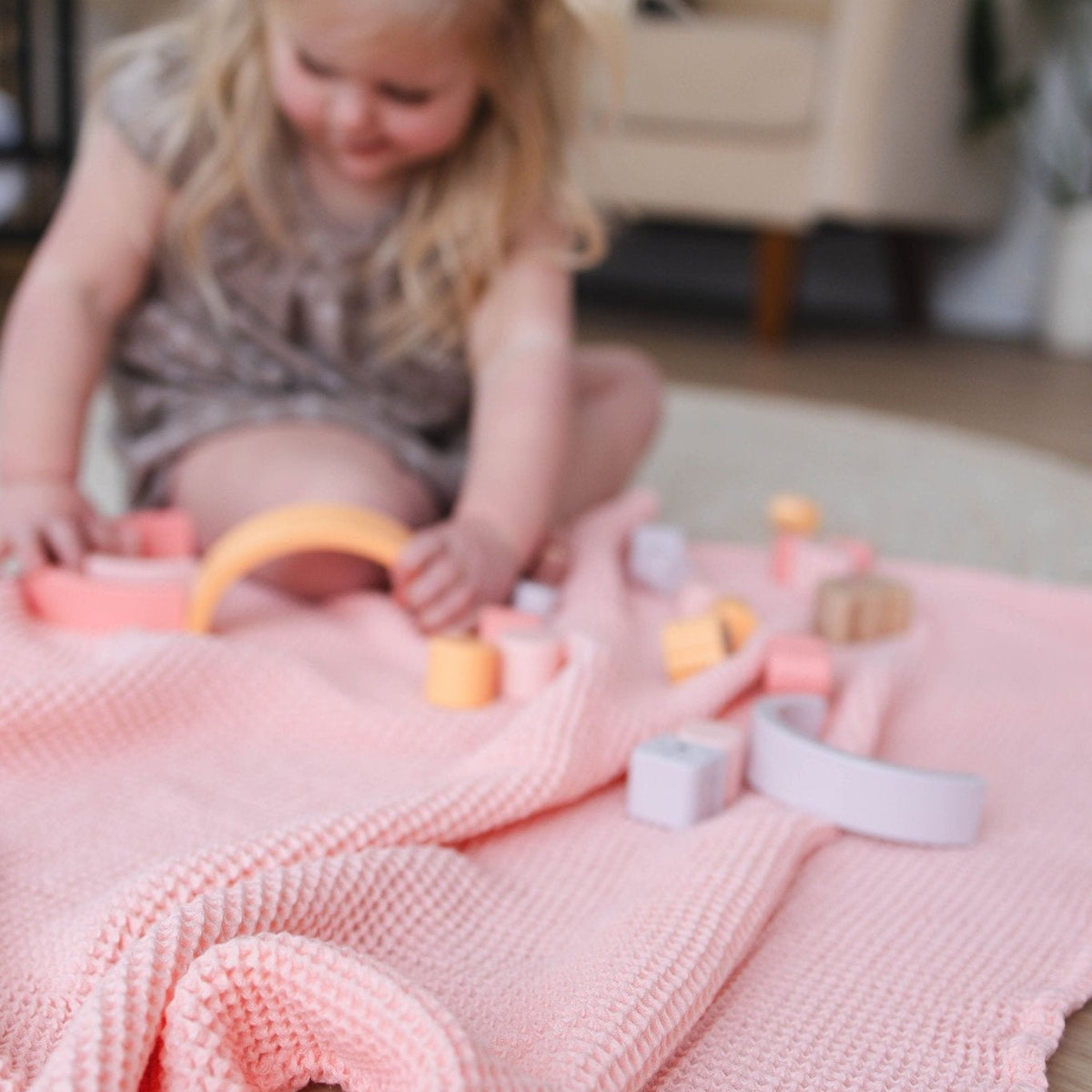 SpiritnSprout: Child playing with stacking toys on a rose pink blanket