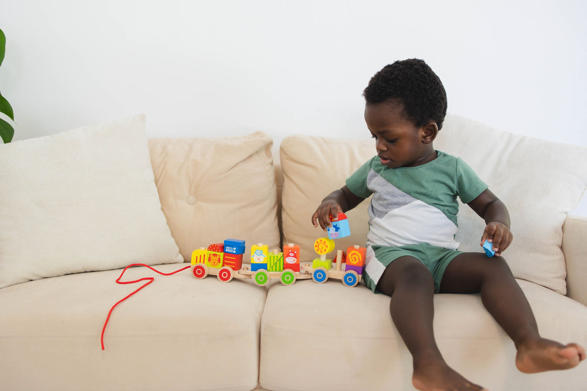 SpiritnSprout: Child playing with the train while seated on a sofa